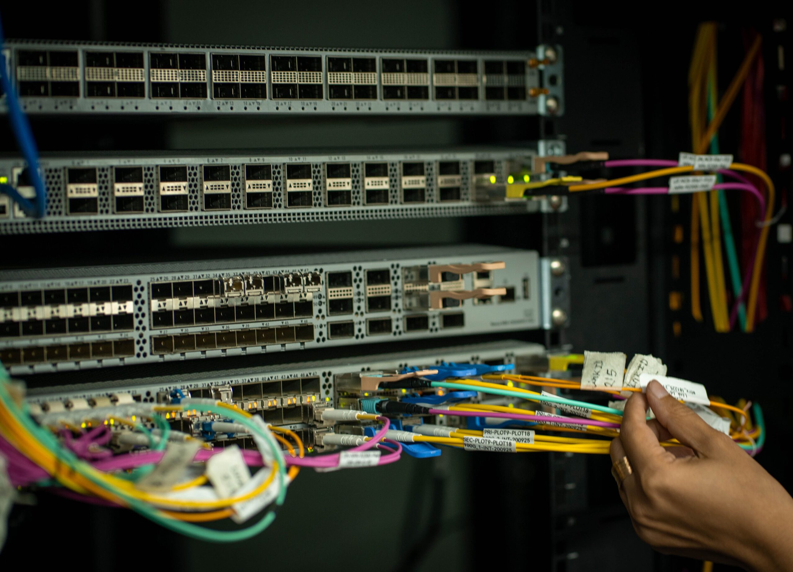 A hand managing fiber optic cables in a server room, showcasing modern connectivity.